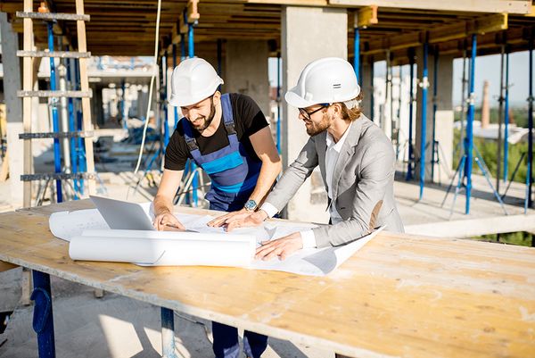 Engineers in hard hats reviewing building plans on site